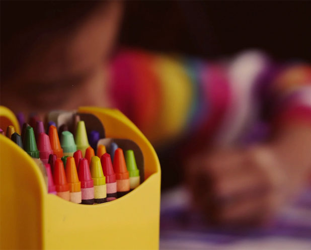 A child sits in front of a yellow box filled with colorful crayons